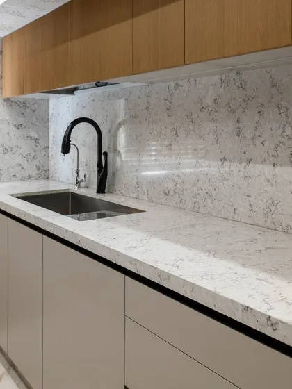 The seamless integration of the sink and the dark faucet against the light quartz countertop adds a touch of modern sophistication. The handleless lower cabinets maintain the clean, linear aesthetic of the space.