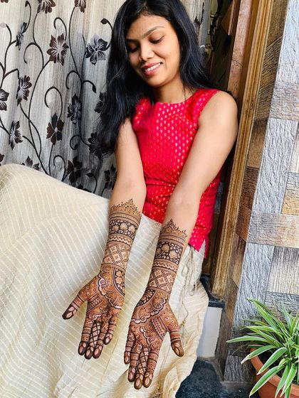 A client enjoying her beautifully intricate mehndi. The design extends up her arms with traditional check patterns and floral bands, showing how stunning a full set can look.