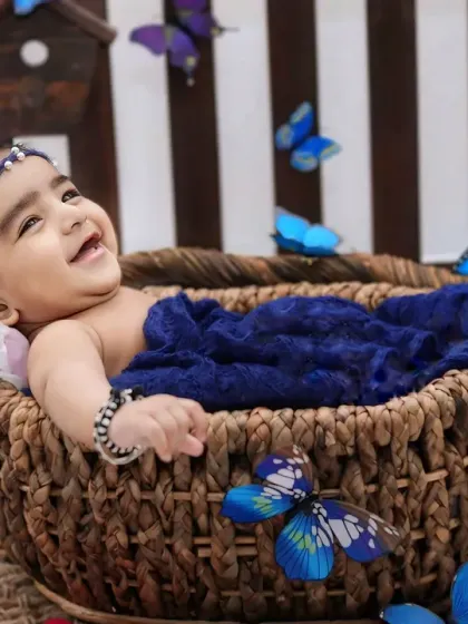 A moment of pure joy as a baby laughs while lying in a basket, with blue butterflies seeming to flutter all around.