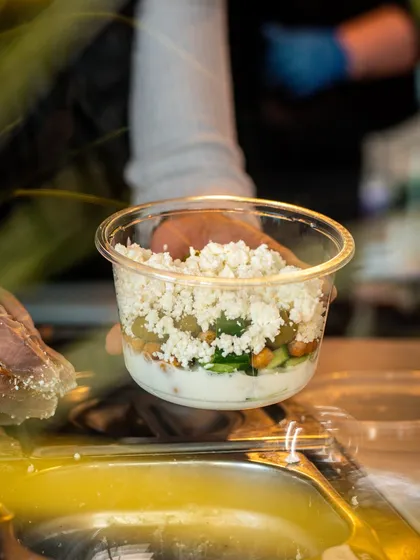 A chef preparing a salad pot to-go. This behind-the-counter shot gives a glimpse into the care taken with every order, even for takeaway.