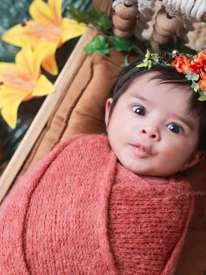A newborn wrapped in a warm, coral-colored swaddle with a floral headband. The date block marks the exact day, creating a personalized and precious memory.