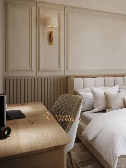 This bedroom includes a dedicated workspace with a quilted chair, perfectly integrated next to the bed against a backdrop of classic wall paneling and a modern sconce.