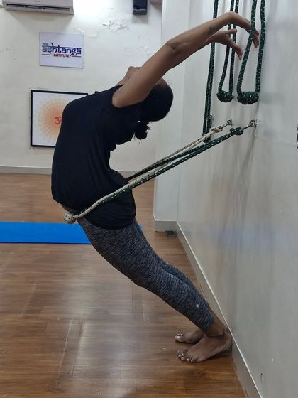 A student performs a supported backbend using the rope wall. This technique helps to open the thoracic spine and improve posture by allowing a passive, deep stretch.