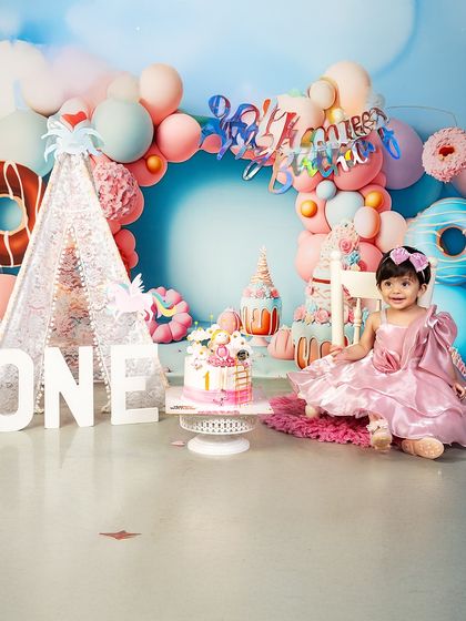 This little princess is ready for her first birthday party! The pink dress and festive donut-themed backdrop create a perfectly sweet and celebratory atmosphere.