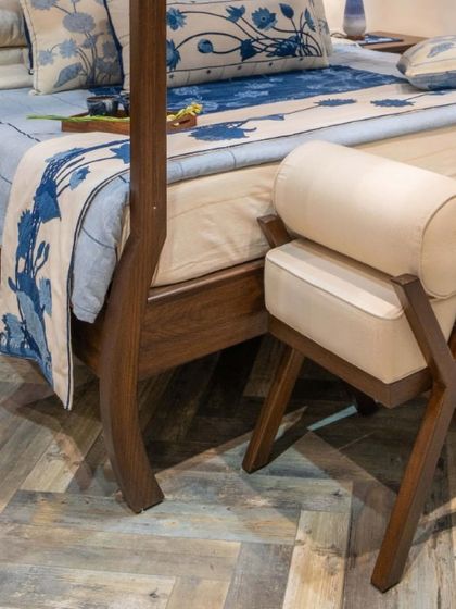 A detail of a bespoke four-poster bed, showing the elegant curve of the wooden leg and the clean lines of the upholstered ottoman. These small, mindful details give our furniture its unique soul.
