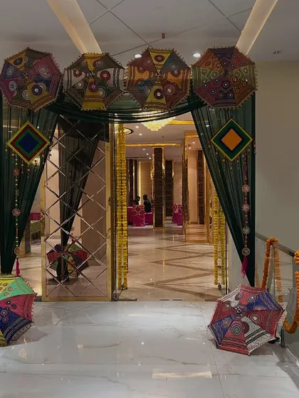 An elegant indoor entrance using dark green drapes and Rajasthani umbrellas, creating a royal welcome for a mehndi or sangeet night.