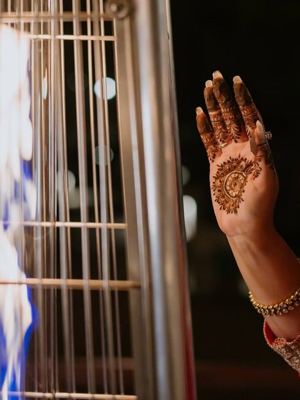 A beautiful detail shot of a bride's hand with intricate henna, warmed by the fire of an outdoor heater.