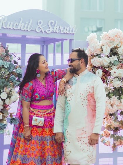 The couple poses at their "Carnival Fiesta" Mehendi, featuring pastel purple decor and a custom photo booth.