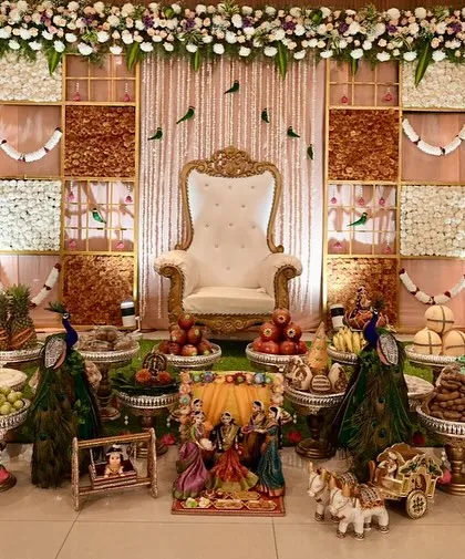A full view of a grand Seemantha setup, featuring a beautiful backdrop with jasmine and marigold panels. The foreground is filled with an elaborate display of traditional sweets and fruits on silver stands, creating a picture of abundance.