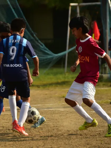 A player skillfully maneuvers the ball between two opponents, demonstrating the close control and composure we develop.