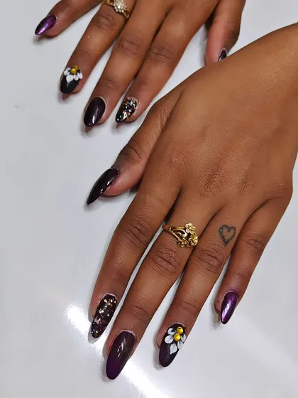 I love adding dimension to my nail sets. Here, I started with a deep, glossy purple base on almond-shaped nails and added hand-crafted 3D flowers with golden centers, complemented by a sparkling glitter accent nail.