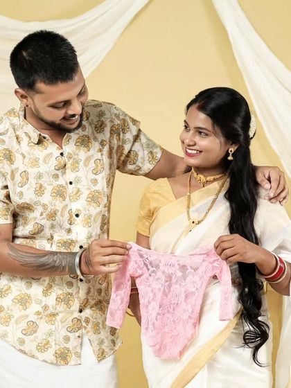 A happy couple reveals they are expecting a girl with a tiny pink outfit. This photo is from our South Indian themed shoot, blending tradition with a joyful announcement.