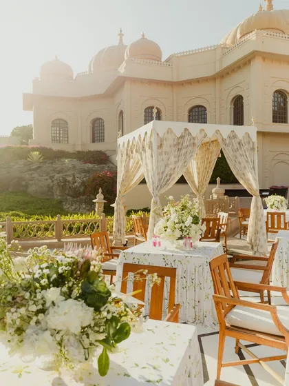 A sun-drenched view of a daytime wedding setup, with elegant canopies and white floral arrangements. The design complements the palace architecture and the natural light.