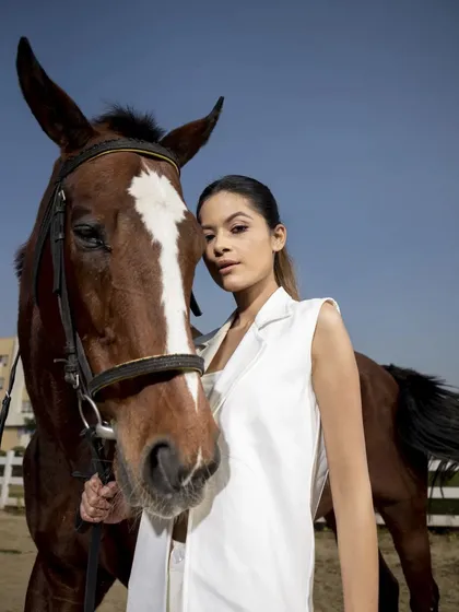 A powerful outdoor portrait of a model in a white sleeveless blazer next to a horse. This image conveys strength and elegance, perfect for a high-fashion editorial.