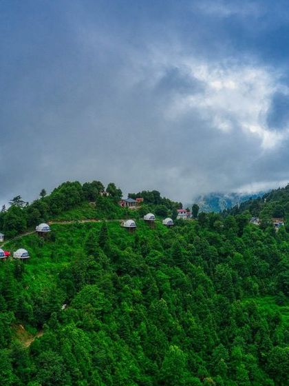 A wide 16:9 aspect ratio shot of the Kanatal domes on the mountainside, perfect for showcasing the expansive natural scenery and the unique layout of the stay.