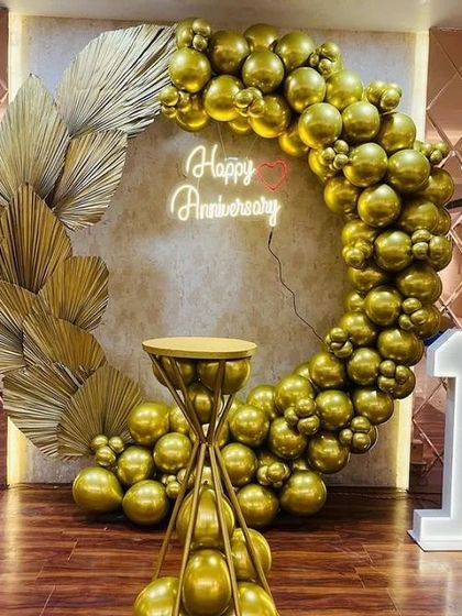 A classic and elegant 1st anniversary celebration. The all-gold balloon ring, accented with dried palm leaves and a neon sign, creates a luxurious and romantic photo spot. The light-up number '1' and custom cake stand complete this beautiful setup.