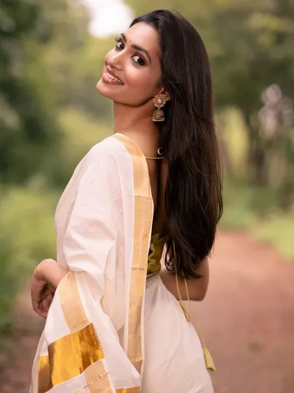 A smiling portrait in a classic white and gold saree, radiating happiness and grace.