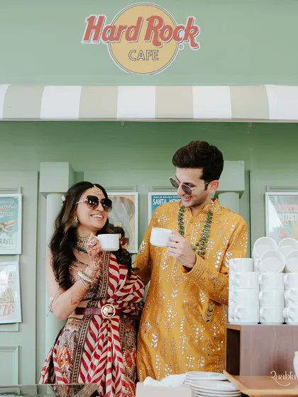 A quirky and cute moment of the couple enjoying a cup of chai at a Hard Rock Cafe themed setup during their haldi event in Jaipur.