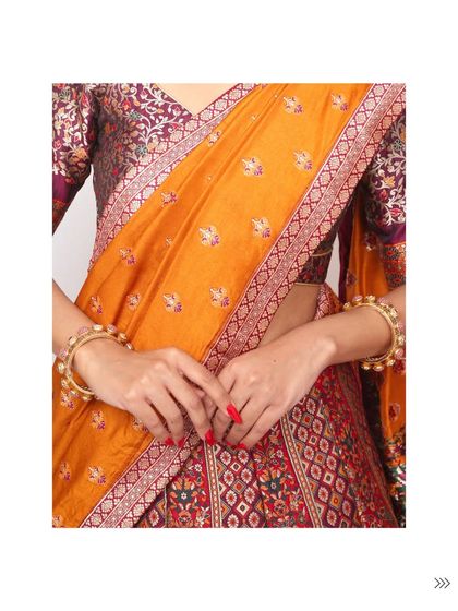 A close-up showcasing the rich textures of a traditional outfit. The vibrant orange patola-style dupatta contrasts beautifully with the brocade blouse and simple bangles.