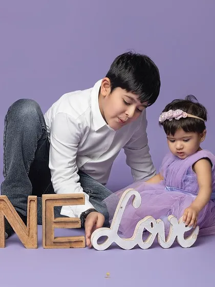 One love. An older brother gently interacts with his baby sister during her first birthday photoshoot, a beautiful moment of sibling connection.