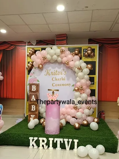 A "Chathi Ceremony" decoration with a pink and rose gold balloon arch. The setup includes "BABY" blocks and an artificial grass floor for a unique look.