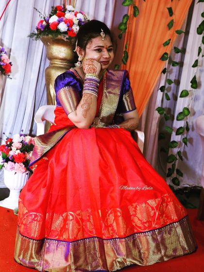 A client ready for her ring ceremony in a vibrant red and blue half saree. Her makeup is bright and celebratory, with henna-adorned hands completing the look.