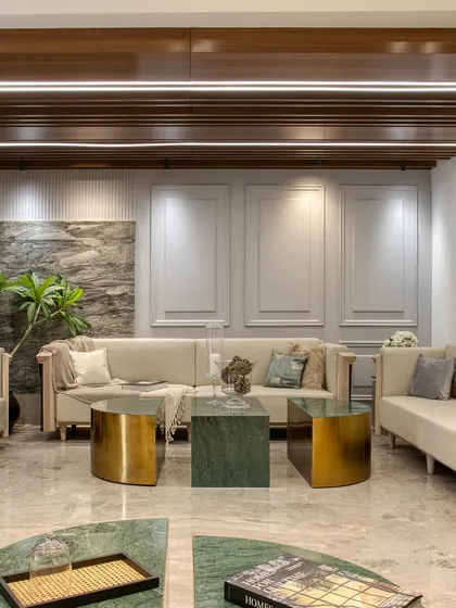 A formal living area designed with neoclassical elements, including wall moldings and custom-built sofas with integrated side tables. The material palette includes marble, wood, and brass for a timeless, elegant feel.
