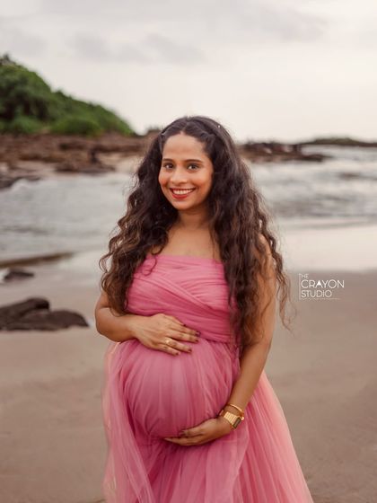 A classic maternity portrait on the beach. She cradles her bump with a warm smile, the soft waves and cloudy sky creating a serene and beautiful backdrop.