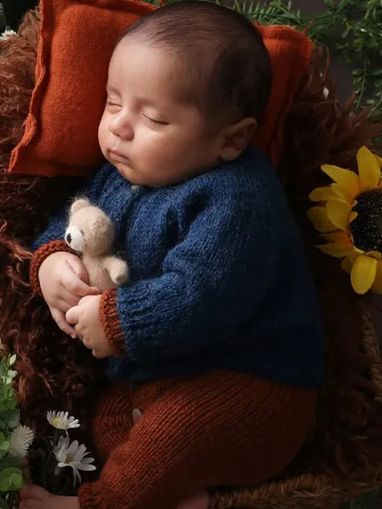 Cradling his tiny teddy. This newborn is posed with a miniature teddy bear, adding a touch of sweetness to the earthy, floral setup. The rich colors of blue and brown create a warm and handsome portrait.