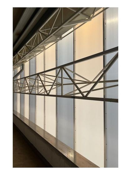 A detail from an industrial project site, showing the translucent polycarbonate wall panels and exposed steel truss work. This image highlights our interest in the honest expression of industrial materials and structural systems.