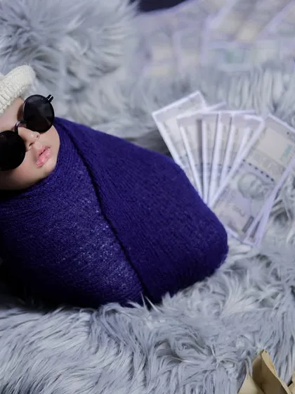 This newborn is ready for his debut. A fun, stylish shot with a swaddled baby in a hat and sunglasses, surrounded by prop money for a "little millionaire" theme.