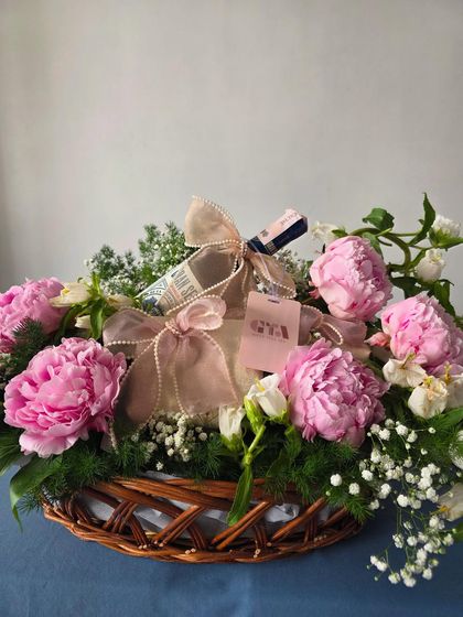 A simple yet stunning hamper featuring a rustic woven basket filled with beautiful pink peonies and a carefully wrapped gift.