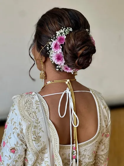 A classic bridal bun adorned with fresh pink and white flowers. This is a beautiful and traditional choice that adds a touch of freshness to the overall look.