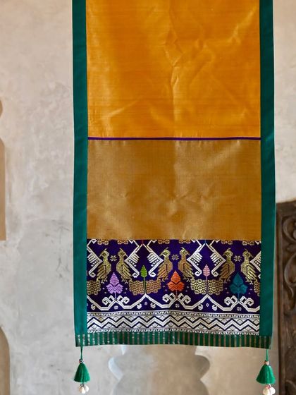 The full length of the golden-yellow runner, highlighting the beautiful contrast between the plain silk body and the intricately woven peacock border.