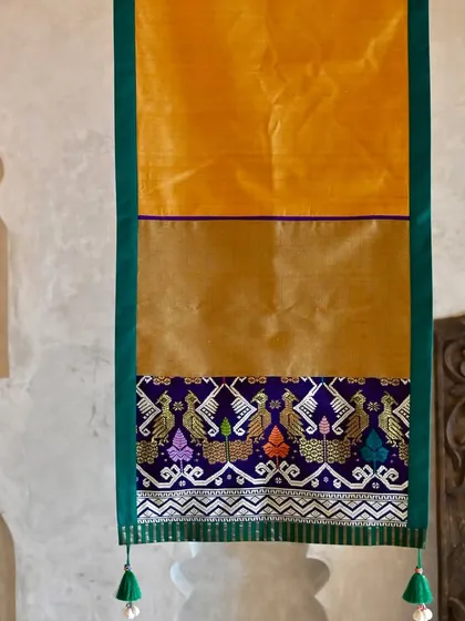 The full length of the golden-yellow runner, highlighting the beautiful contrast between the plain silk body and the intricately woven peacock border.