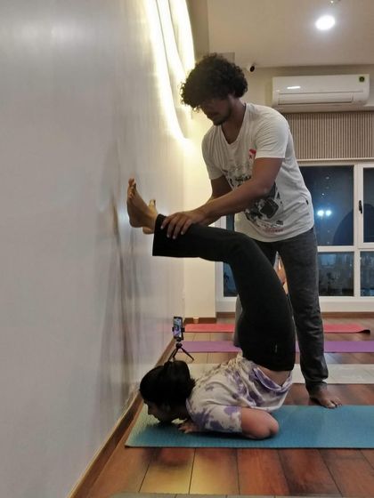 A student receives an adjustment in a forearm stand variation, helping to stabilize the shoulders and find proper alignment.