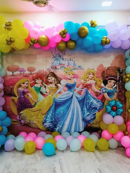 A grand Disney Princess theme featuring a large backdrop with Cinderella, Belle, Rapunzel, and Snow White. The scene is framed by a vibrant, multi-colored balloon arch.