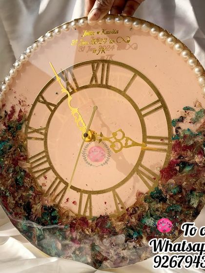 A full view of a custom wedding clock, featuring a pearl border and the couple's names and wedding date. The lower half is filled with a colorful mix of their preserved varmala flowers.