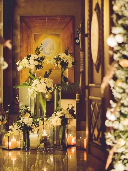 An artfully arranged entryway display. We use varying heights and reflective surfaces to create depth, with candlelight casting a warm glow on elegant white floral bouquets for a truly breathtaking welcome.