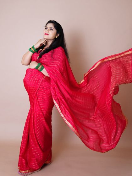 A striking portrait of a mother-to-be in a flowing red saree, captured in a moment of thought and anticipation.