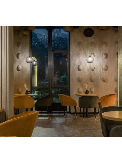 An intimate seating area with mustard and dark green velvet chairs. The textured walls and subtle pendant lighting create a cozy and sophisticated atmosphere for evening dining.