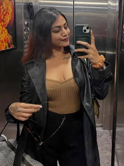 An elevator selfie showing off a chic city look. I've layered a black leather-look trench coat over a neutral top and black trousers for a sophisticated ensemble.