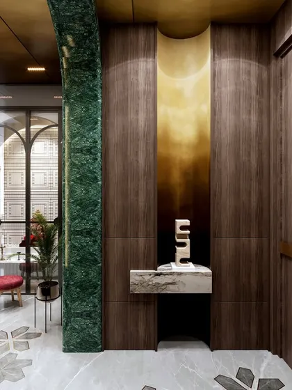 This transitional space features a bold material palette, including rich wood paneling, green marble columns, and a brass-accented niche. The custom-inlaid marble floor and arched doorways create a sense of grandeur and a seamless flow into the main living areas.