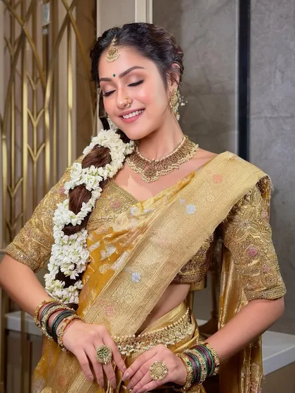 A joyful, smiling portrait that captures the bride's happiness. The makeup is radiant and enhances her natural beauty, perfectly complementing the traditional gajra braid and gold jewelry.