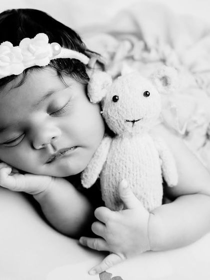 A timeless black and white close-up. This image focuses on the peaceful expression of a sleeping newborn cuddling a small knitted toy, emphasizing emotion and detail.