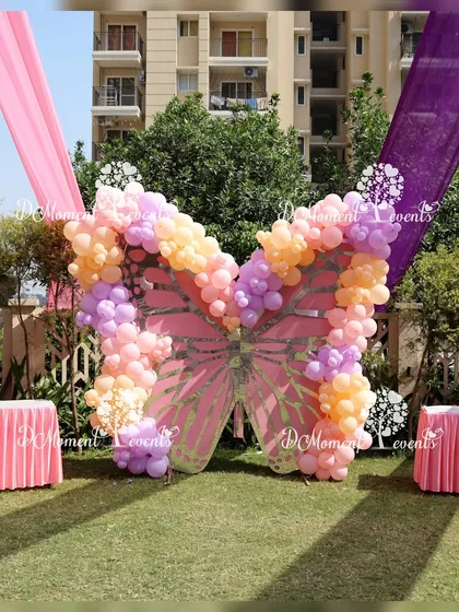 A large butterfly-shaped balloon mosaic stands as a stunning photo backdrop on the green lawn of an outdoor party.