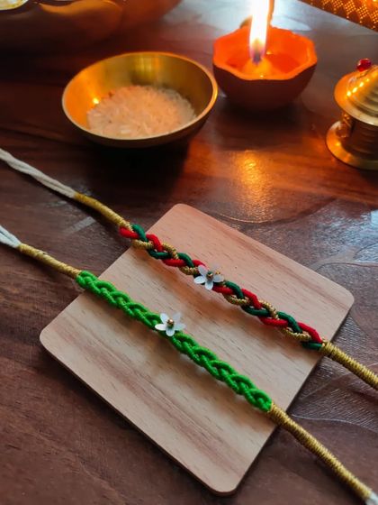 These braided rakhis are a unique option for the festival. They are available in a green braid and a red-and-green braid, each with a small floral charm.