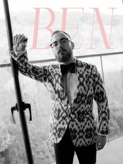 A stylish black and white portrait of the groom, Ben. His modern ikat-patterned jacket and confident pose against the window create a very editorial, high-fashion look.
