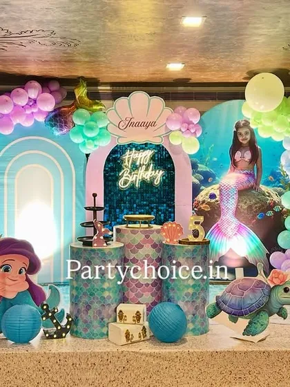 The main stage for our mermaid theme, featuring character cutouts of Ariel, an under-the-sea backdrop, and balloon arches in shades of blue, purple, and green to mimic ocean waves.