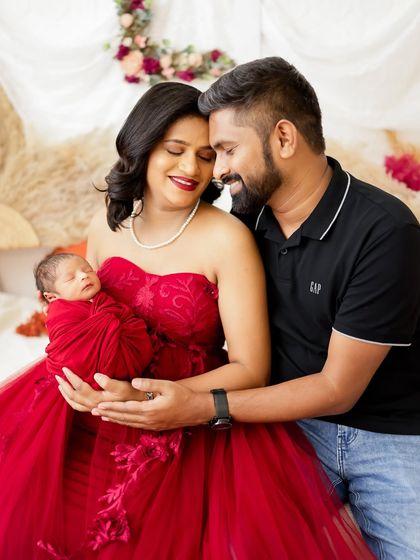 A beautiful family of three, with the parents lovingly holding their newborn. The mom's red dress creates a vibrant and passionate feel.